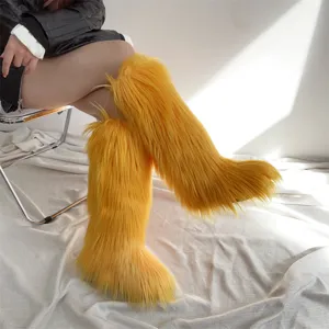 Close-up view of bright yellow knee-high faux fur snow boots worn by a model in a minimal studio.
