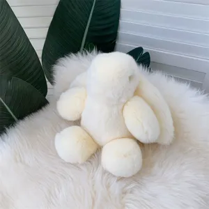 Gros plan d'un lapin en peluche crème doux sur un tapis de fausse fourrure blanche doux.
