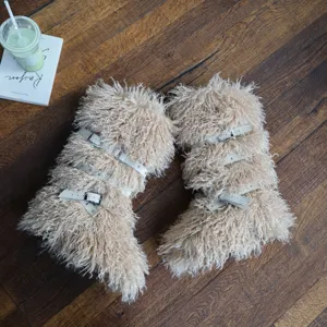 Dettaglio di stivali da neve beige in ecopelliccia con cinturini e fibbie bianche su legno