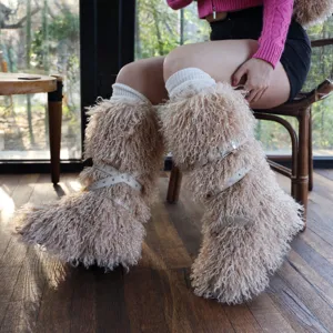 Dettaglio di stivali da neve beige pelosi con cinturini incrociati in pelle e borchie.