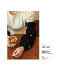 Detail of black cotton oversleeves with floral embroidery worn in a cozy cafe setting