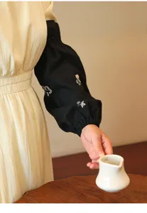 Close-up of black cotton arm covers with floral embroidery in a lifestyle setting.