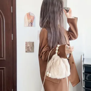 Nahaufnahme der beigefarbenen Faux-Nerz-Eimertasche mit elegantem Perlengriff.