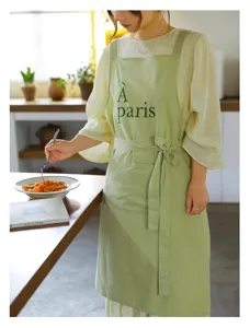 Dettaglio del grembiule in cotone verde chiaro con ricamo À Paris in una cucina accogliente.