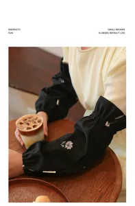 Detailed macro view of black embroidered oversleeves in a cozy cafe lifestyle setting