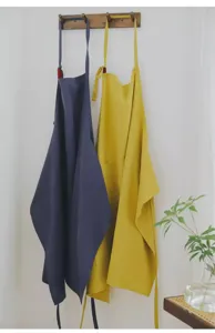 Vista lifestyle di grembiuli senza maniche in cotone blu e giallo senape su un appendino in legno