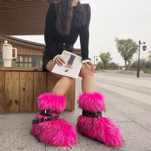 Close-up of bright pink faux fur snow boots with black straps and studs worn by a model.