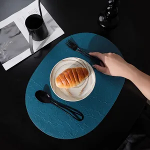 Elegante tovaglietta ovale blu navy in pelle con piatto di marmo e croissant sul tavolo