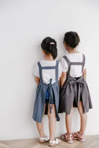 Vista trasera de dos niños con delantales de algodón azul y gris sobre pared blanca