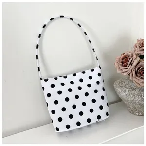 Detalle de bolso bajo el brazo de nailon blanco con lunares negros en fondo minimalista