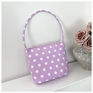 Detalle de un bolso de nylon morado con lunares blancos sobre un estante blanco