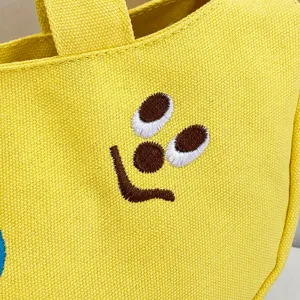 Makroaufnahme einer süßen Cartoon-Stickerei auf einer gelben Segeltuch-Aufbewahrungstasche.