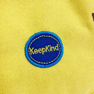 Makrodetail des KeepKind-Stickpatches auf einer gelben Segeltuch-Kindertasche