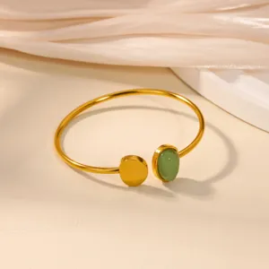 Detailed shot of an open gold stainless steel bracelet with green stone and disc.