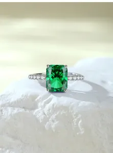 Detailfoto van een smaragdgeslepen groene edelsteenring met steentjes op witte rots.