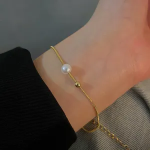 Delicate detail shot of minimalist gold snake chain bracelet with pearl and metal bead.