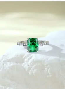 Detailopname van ring met groene steen in smaragdgeslepen stijl op witte steendisplay.