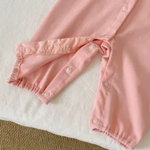 Détail de grenouillère rose pour bébé, tissu côtelé doux avec boutons-pression pratiques.