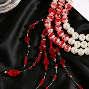 Detailed close-up of Y-shape pearl necklace with red marble beads on black silk.