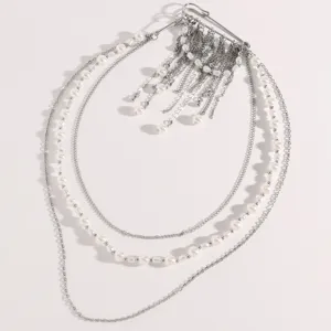 Vista detallada de un broche de múltiples capas plateado con perlas y cadenas de borlas