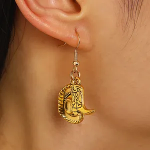 Close-up of golden western cowboy hat and boot charm dangle earrings worn on ear.