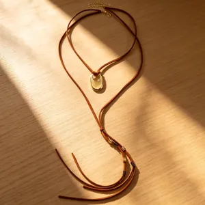 Nahaufnahme einer braunen Vintage-Kordelkette mit goldenem U-Anhänger auf Holz