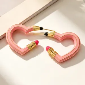 Nahaufnahme von rosa herzförmigen Ohrringen mit kreativem Bleistiftdesign und Goldakzenten