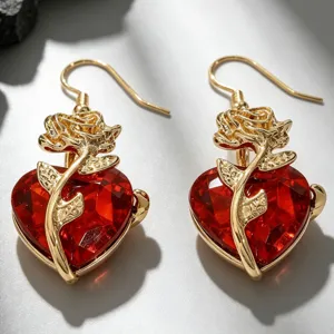 Gros plan de boucles d'oreilles rose dorée gothique autour d'un cœur en cristal rouge.