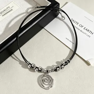 Close-up detail of a silver-tone swirl rose pendant necklace on a black waxed cord