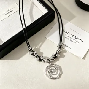 Detail of a vintage silver rose swirl pendant on a black cord with metallic beads.