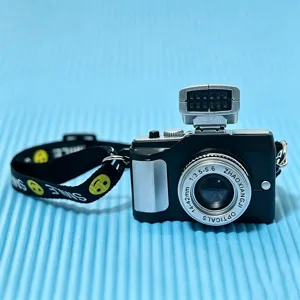 Close-up of a miniature black camera accessory with a yellow smiley face smile strap