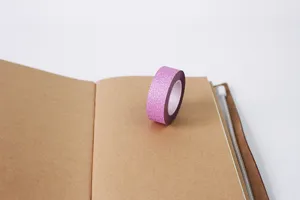 Detail shot of a sparkling pink washi tape roll placed on a blank brown notebook page.