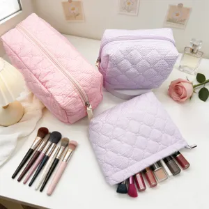 Detailed view of quilted cosmetic bags and makeup brushes neatly arranged on a clean white table.