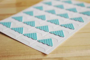 Vue détaillée de coins photo à grille bleue sur fond bois, parfaits pour albums de scrapbooking DIY.