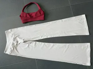 Detailansicht des Yoga-Sets mit rotem Halter-Top und weissen Schlaghosen fuer Sport.
