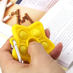 Detail view of yellow silicone star push pop fidget toy keychain held in hand for stress relief.