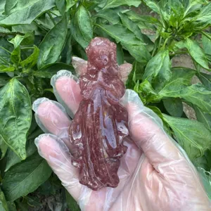 Detail shot of a hand holding a 10cm carved crystal angel gemstone sculpture outdoors.
