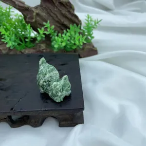 Close-up detail of a mini natural stone carved crystal cat figurine on dark wooden base.