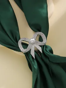 Primo piano dettagliato dell'anello per foulard con fiocco in strass e perla su raso verde.