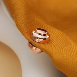 Detaillierte Nahaufnahme eines runden roségoldenen magnetischen Schalclips auf gelbem Stoff.