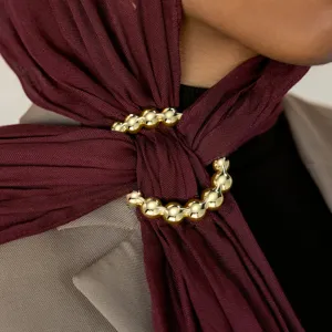 Close-up detail of luxurious gold bead scarf ring worn on maroon hijab, elegant accessory.