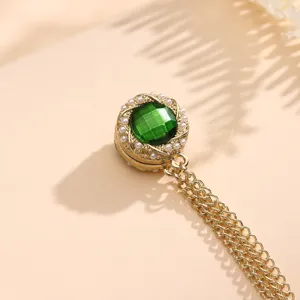 Gedetailleerd zicht op gouden vintage magneetbroche met groene edelsteen en kettingen.