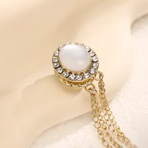 Gedetailleerde opname van gouden magnetische broche met witte kattenoog en kettinkjes.
