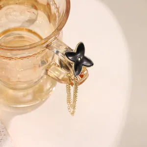 Close-up detail of black camellia magnetic buckle accessory with gold chains on cup handle.