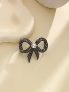 Primo piano del dettaglio della fibbia per sciarpa a fiocco scuro con strass e perla.