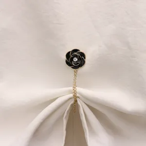 Close-up detail of black camellia flower magnetic buckle with gold chain on white fabric.