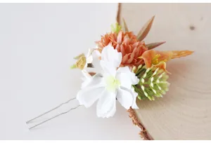 Close-up detail of a pastoral style floral hair pin with white and orange artificial flowers.