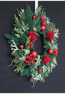 Detailed close-up shot of artificial Christmas wreath with red roses, berries, and pine.