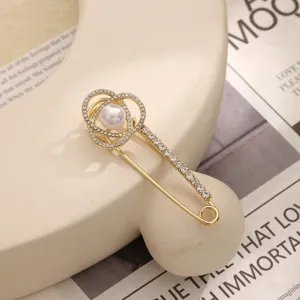 Gold safety pin brooch with dazzling rhinestones and a pearl accent for elegant outfit styling.