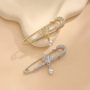 Rhinestone safety pin brooch detail, elegant pearl pendant, gold and silver fashion accessory decor.
